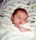 Baby reclining on colorful pillow wrapped in blanket looking off camera