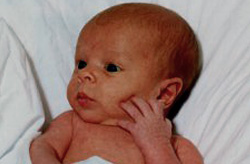 Close up of newborn looking off camera with hand on face