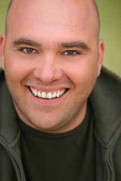 A smiling man in his 30s sitting in front of a green background